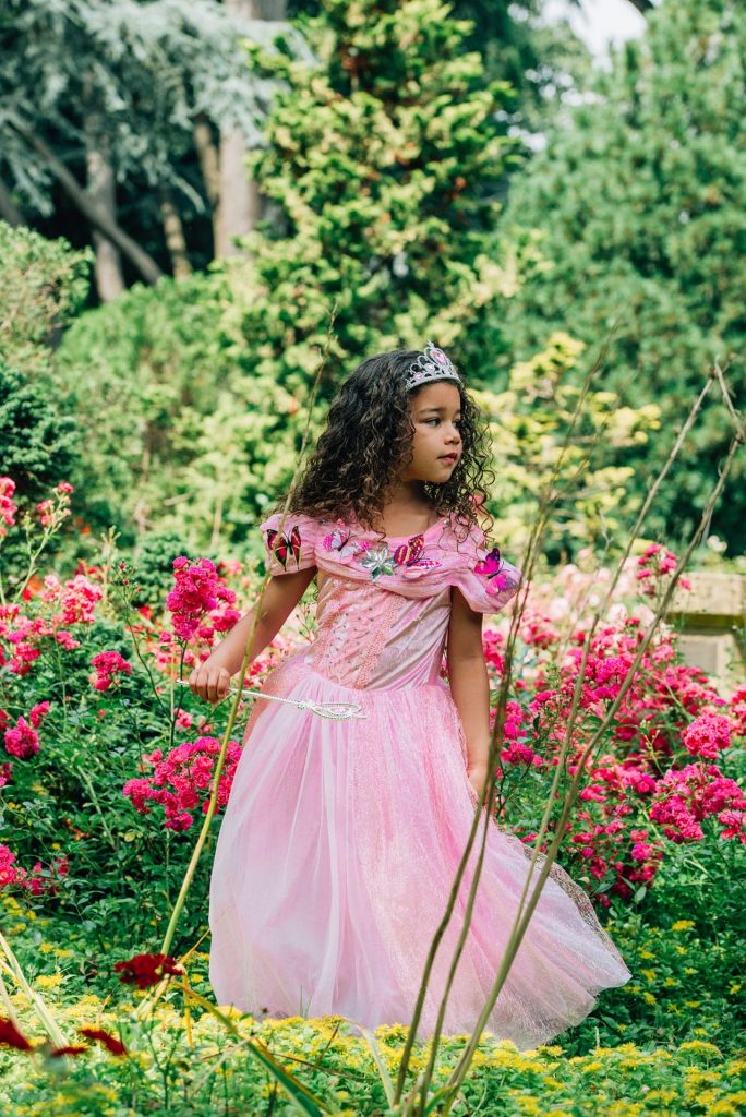Meisje in een roze prinsessenjurk die rent in de tuin met een toverstaf